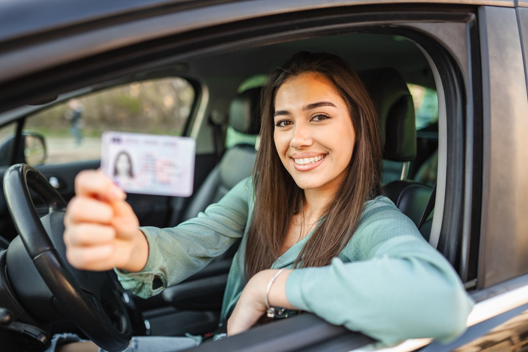 Portrait of a smiling young woman sitting in the drivers seat holding drivers license